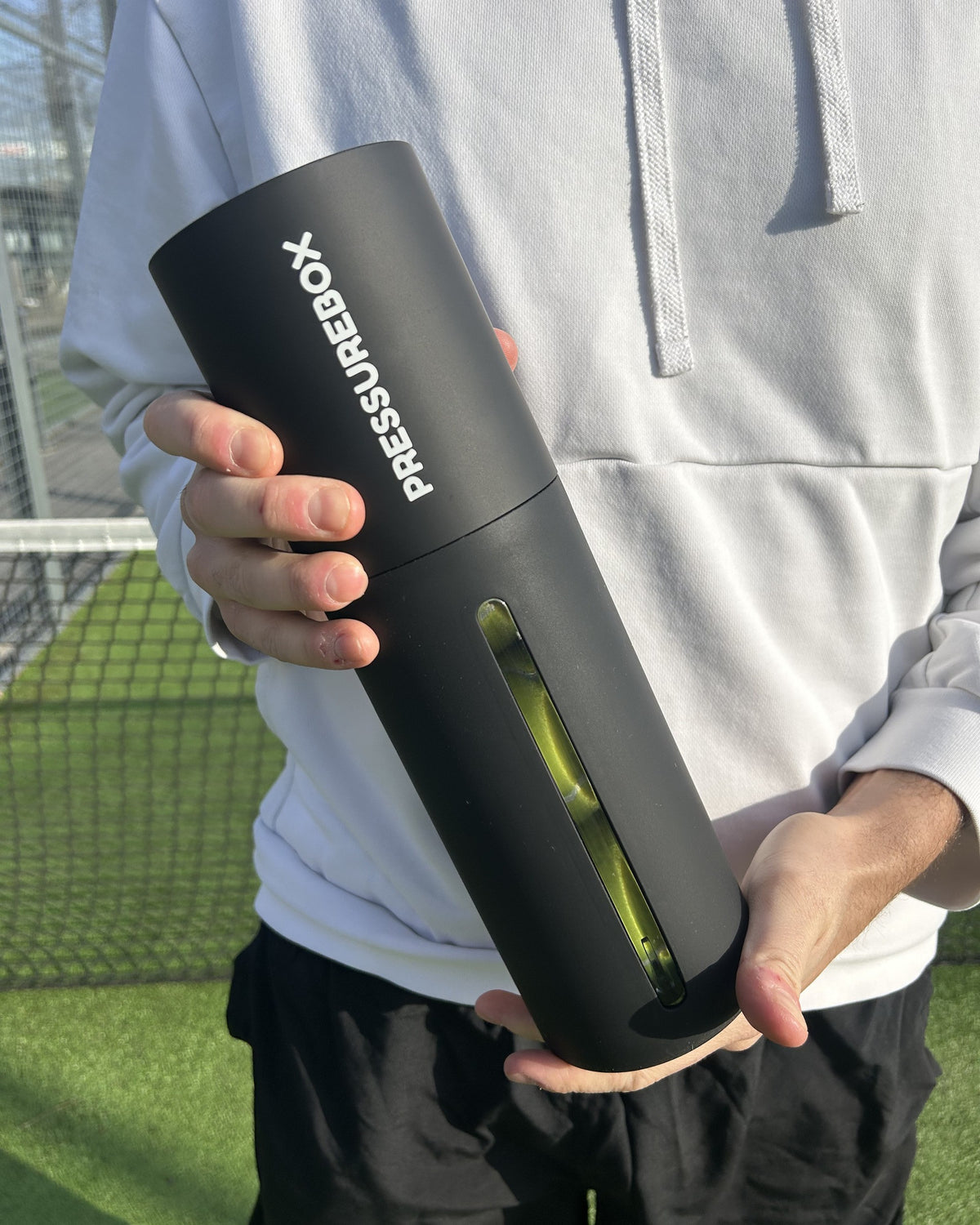 A padel player holding a Pressurebox Pro Padel automatic ball pressurizer with three balls inside, on an outdoor padel court