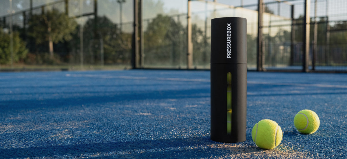 Pressurebox Pro Padel automatic ball pressurizer on a blue padel court next to two padel balls