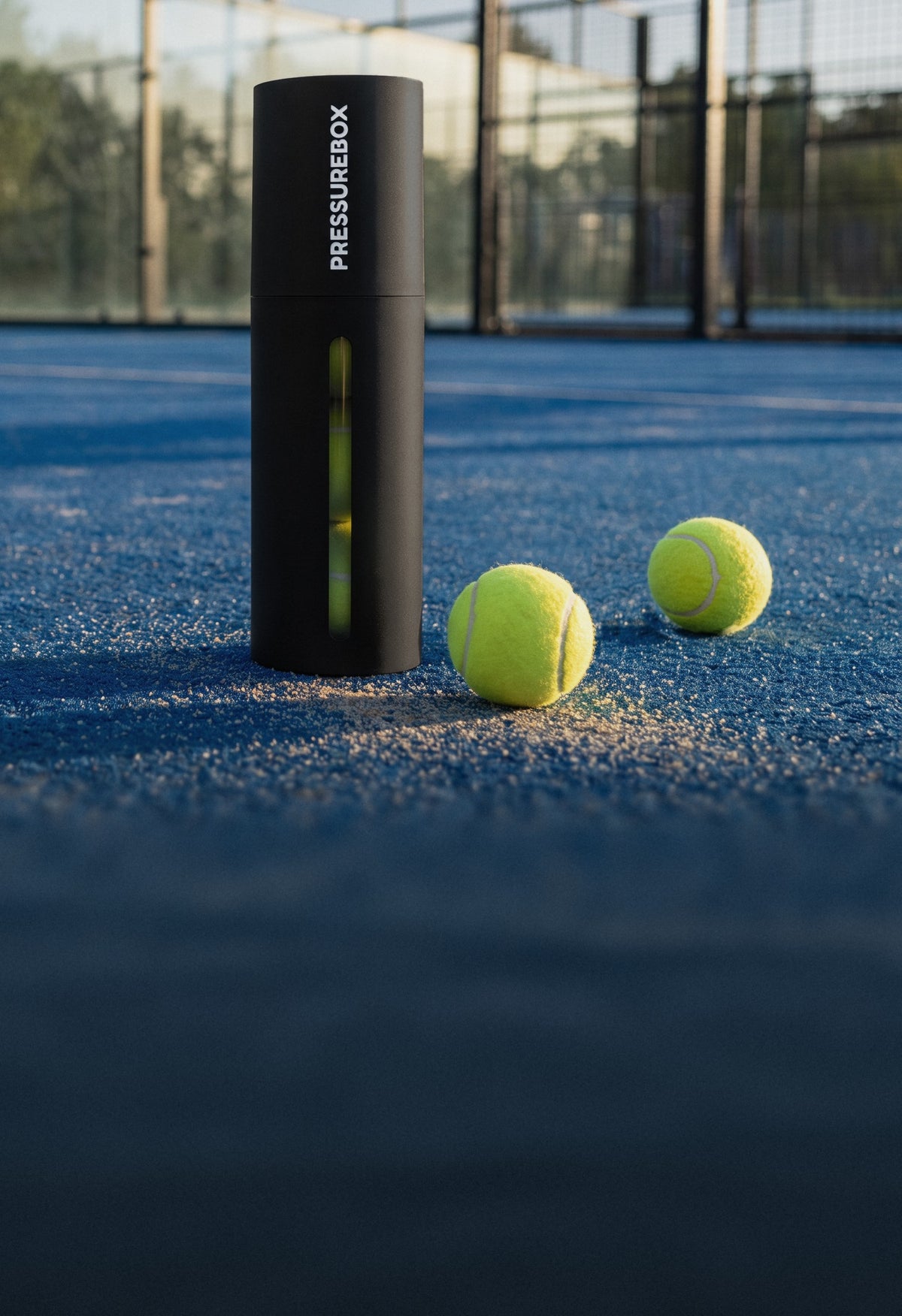 Pressurebox Pro Padel automatic ball pressurizer on a blue padel court next to two padel balls